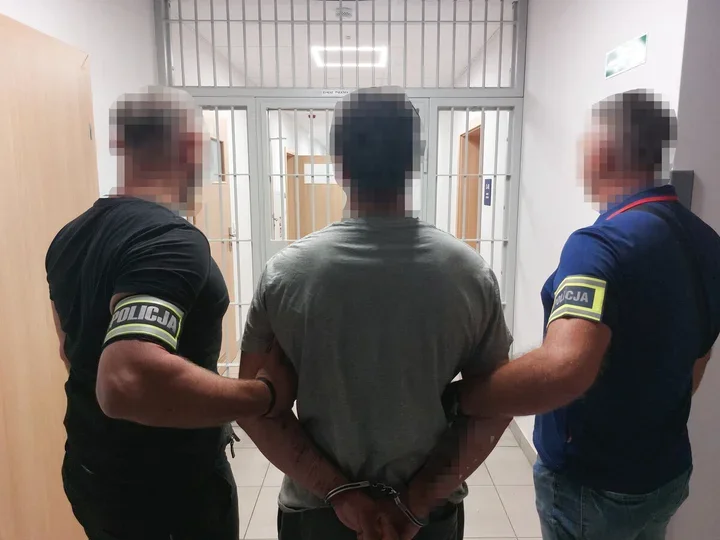 Dwóch policjantów prowadzi zakutego w kajdanki mężczyznę do celi w jednostce policji.